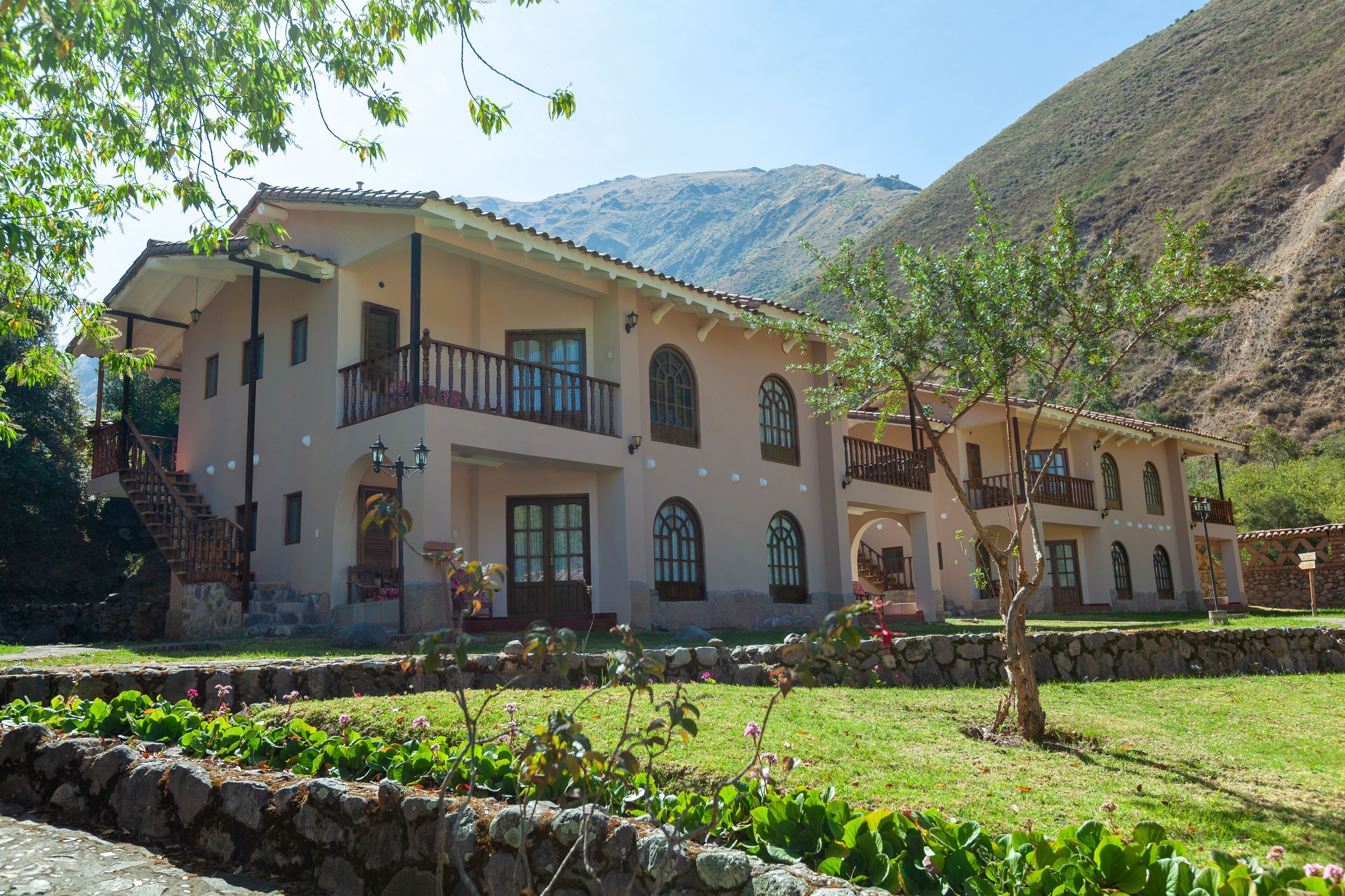 A two-story building with a balcony, stone walls, and a mountainous backdrop.