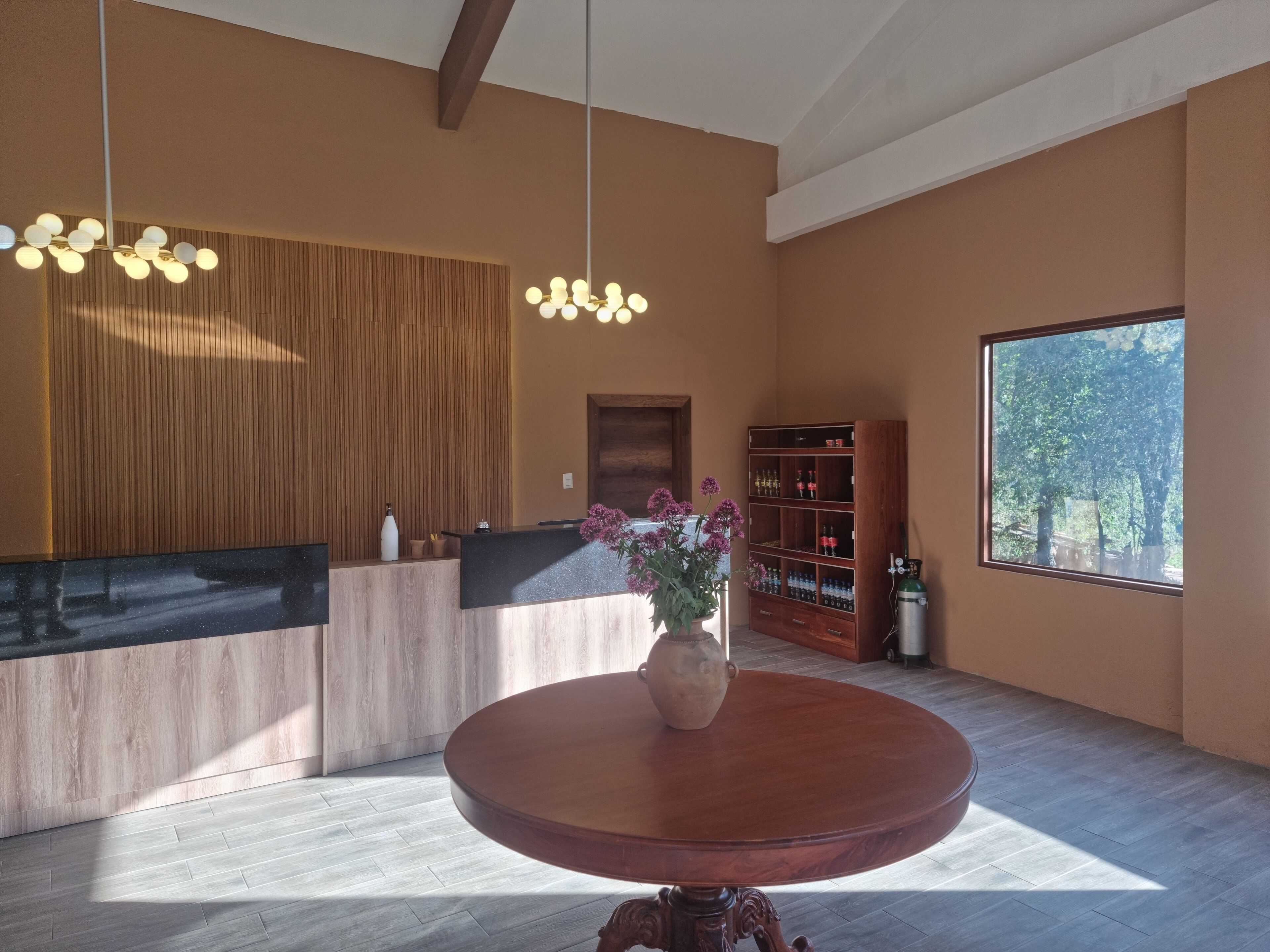 Un'accoglienza moderna con una scrivania in legno, un tavolo rotondo in legno con un vaso di fiori e una libreria piena di bottiglie.