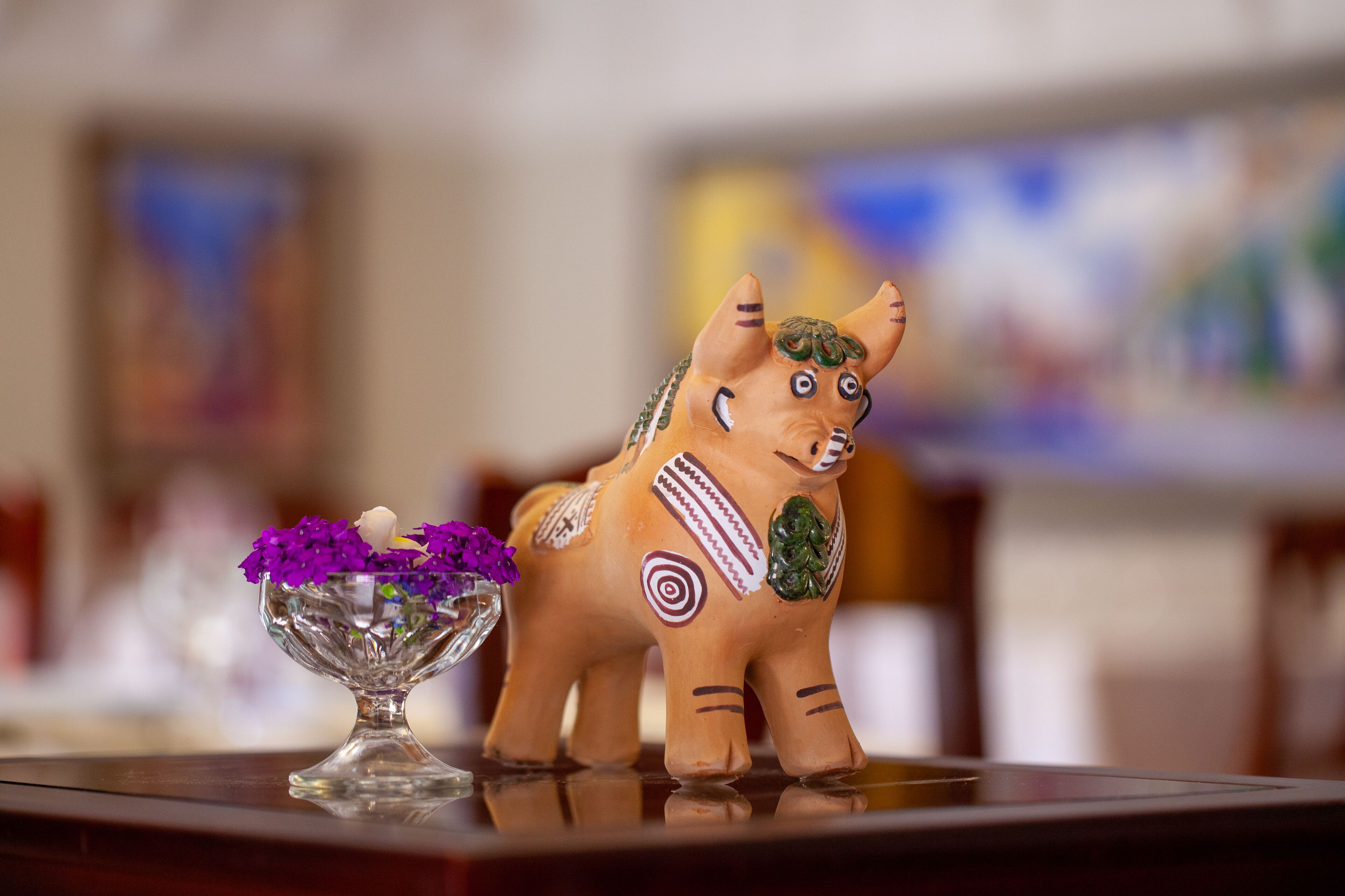 A ceramic elephant figurine with decorative patterns and a glass bowl with purple flowers on a reflective surface.
