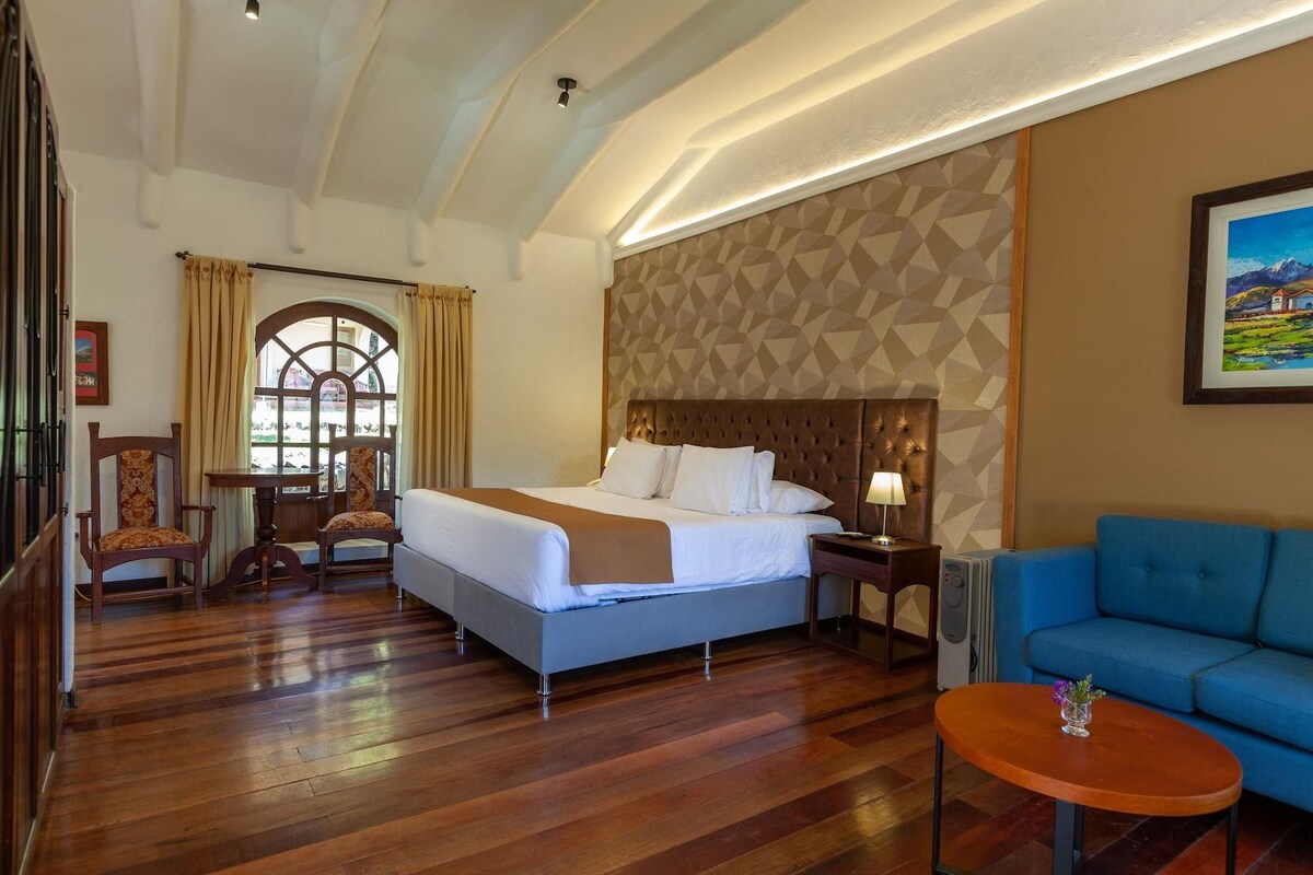 A hotel room with a large bed, a blue sofa, a wooden floor, and a patterned wall.