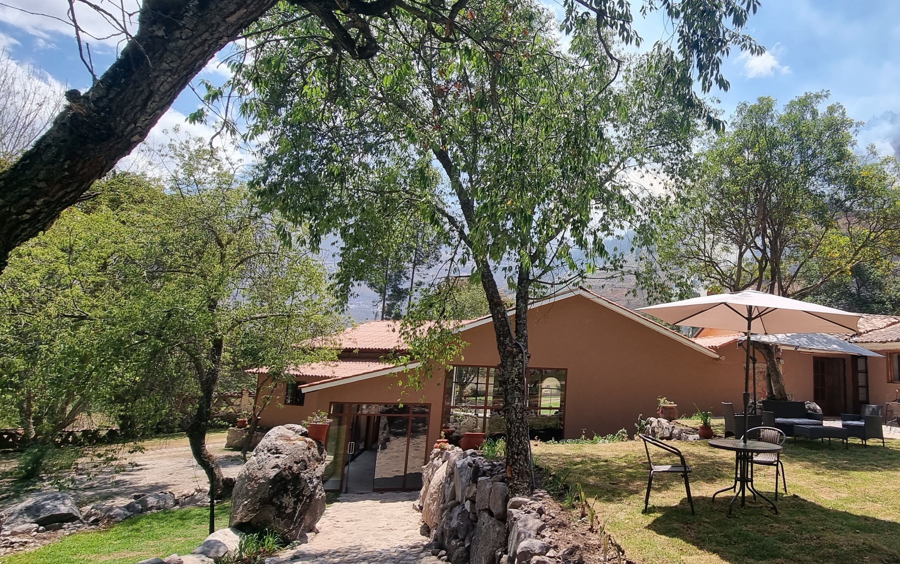 Una casa con techo de tejas, un patio con mesa y sillas, y vistas a los árboles y el paisaje circundante.
