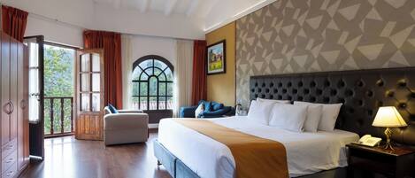 Habitación de hotel con una cama grande, un sofá, una mesa de comedor y vistas al exterior.