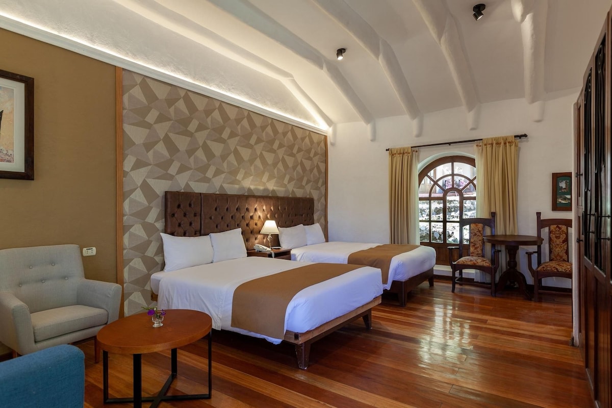 A hotel room with two beds, a sofa, a small table, and a window with curtains.