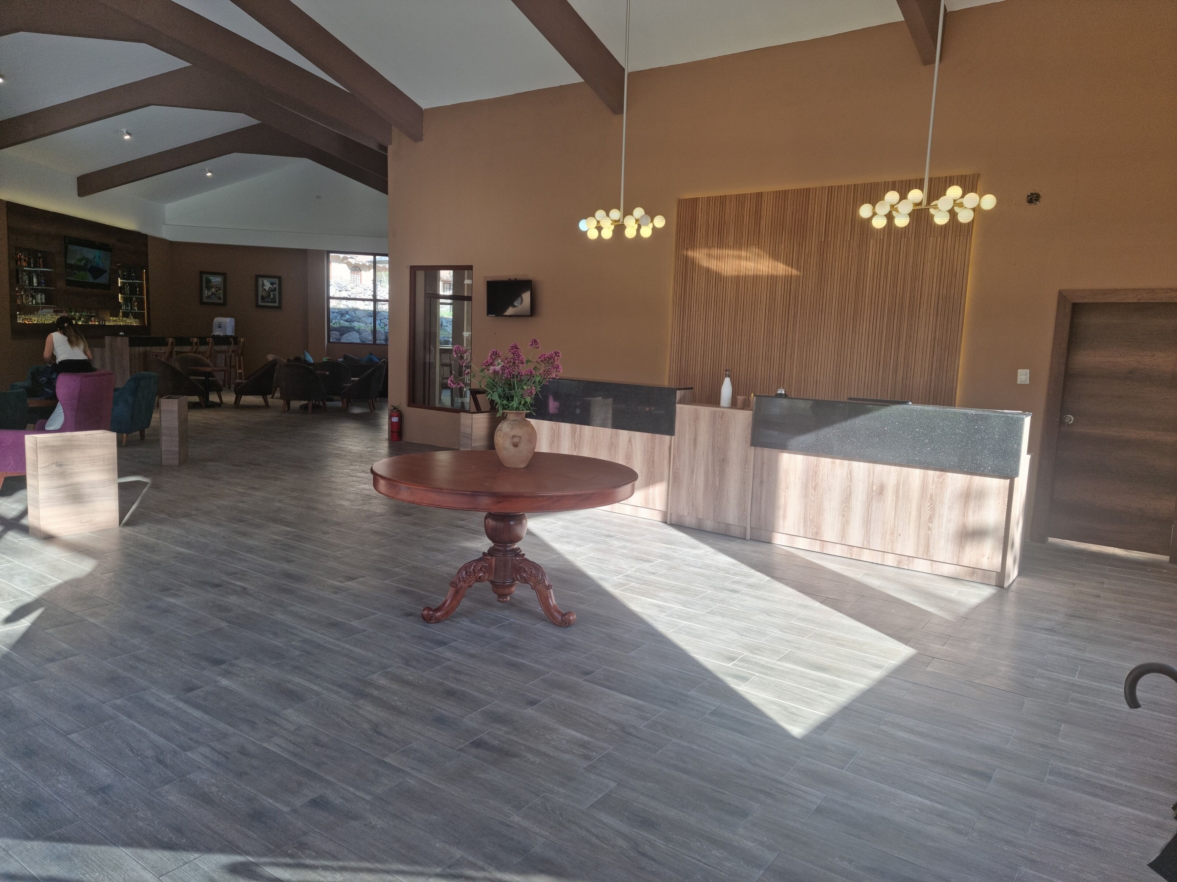 Un vestíbulo amplio con un mostrador de recepción de madera, una mesa redonda de madera y una zona de bar al fondo.