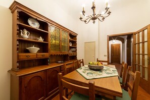 Une salle à manger avec une table en bois, des chaises, un lustre et un buffet rempli de vaisselle.