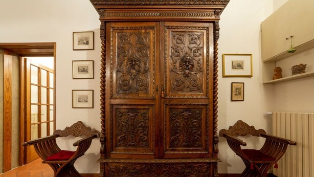 Une pièce comprenant un grand buffet en bois sculpté, deux chaises en bois avec des coussins rouges et des tableaux encadrés accrochés au mur.