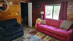 A cozy room with a wooden ceiling, a red sofa, a blue armchair, and a patterned rug. - Cabin 8 miles from Kings Canyon entrance gate. (Miramonte)