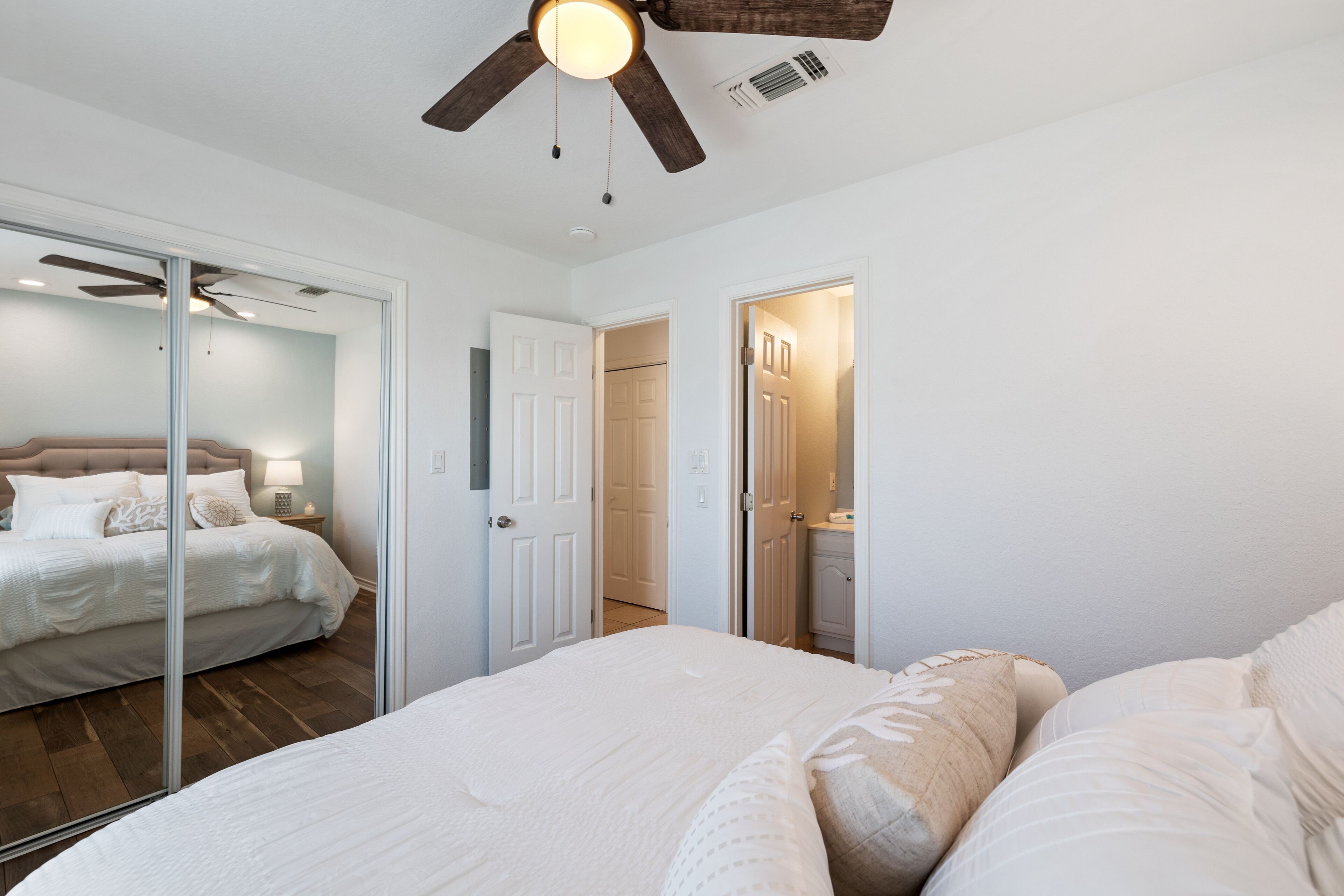 A bedroom with a bed, a ceiling fan, and a door leading to another room.