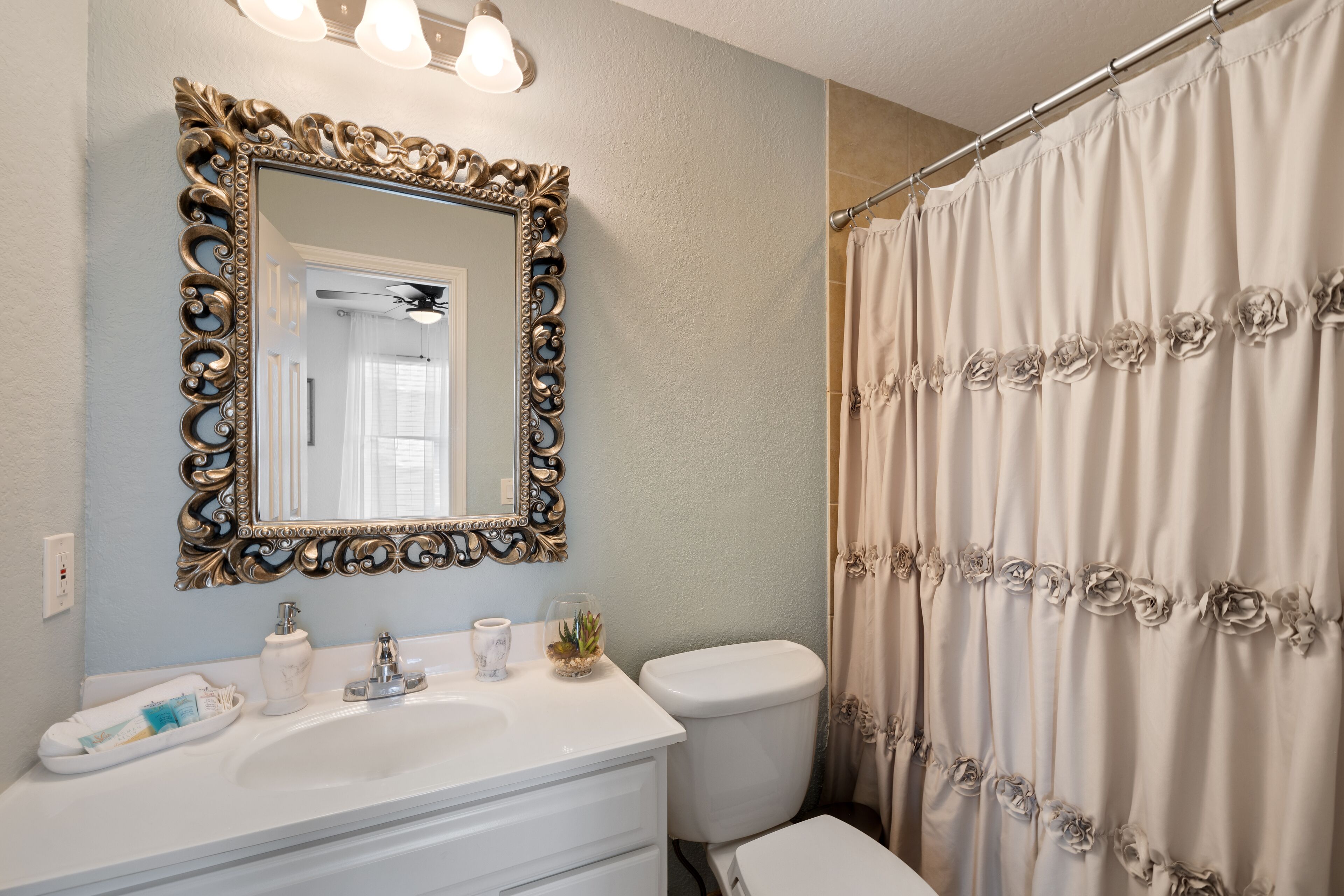 A bathroom with a white sink, a toilet, and a shower curtain with floral patterns.