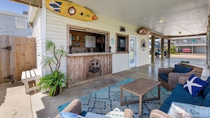 A covered outdoor seating area with a wooden table, wicker furniture, and a surfboard decoration.