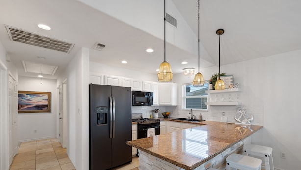 A modern kitchen with white cabinets, a granite countertop, and pendant lighting.