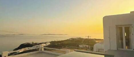 A modern infinity pool with a view of the sea and distant land during sunset.