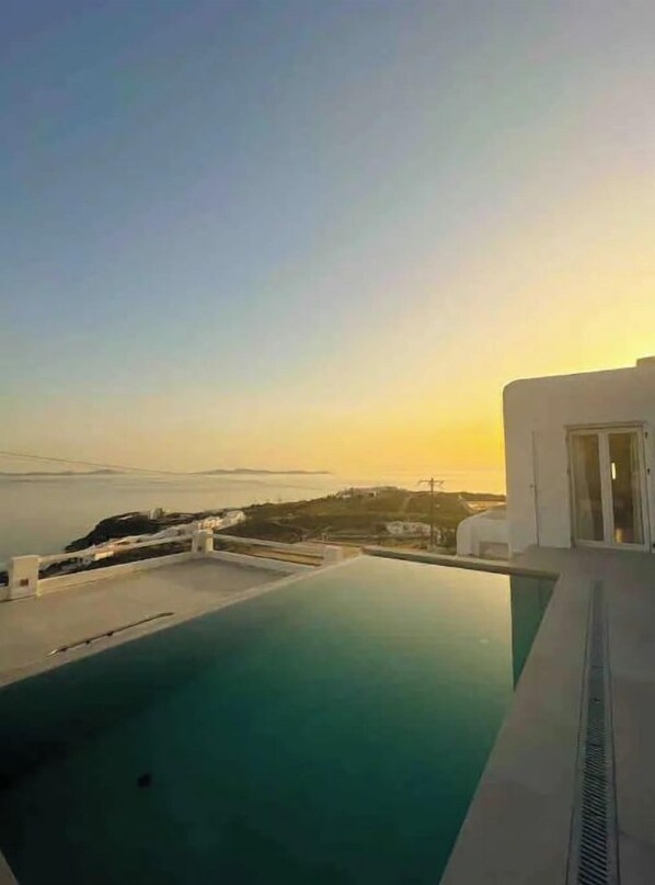 Une piscine à débordement moderne offrant une vue sur la mer et le paysage lointain au coucher du soleil.