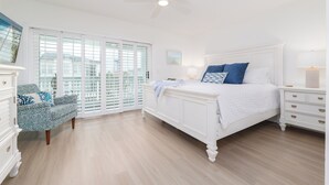 Een slaapkamer met een wit bed, nachtkastje, dressoir en een stoel.