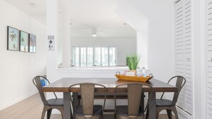 Een eetruimte met een houten tafel, vier metalen stoelen, een plant op tafel en een raam met zonwering.