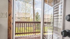 A wooden deck with a metal railing, a glass door, and a view of a grassy yard with trees. - Teton National Park Avails! Great Location, Games, Laundry, & Playround! (Driggs)