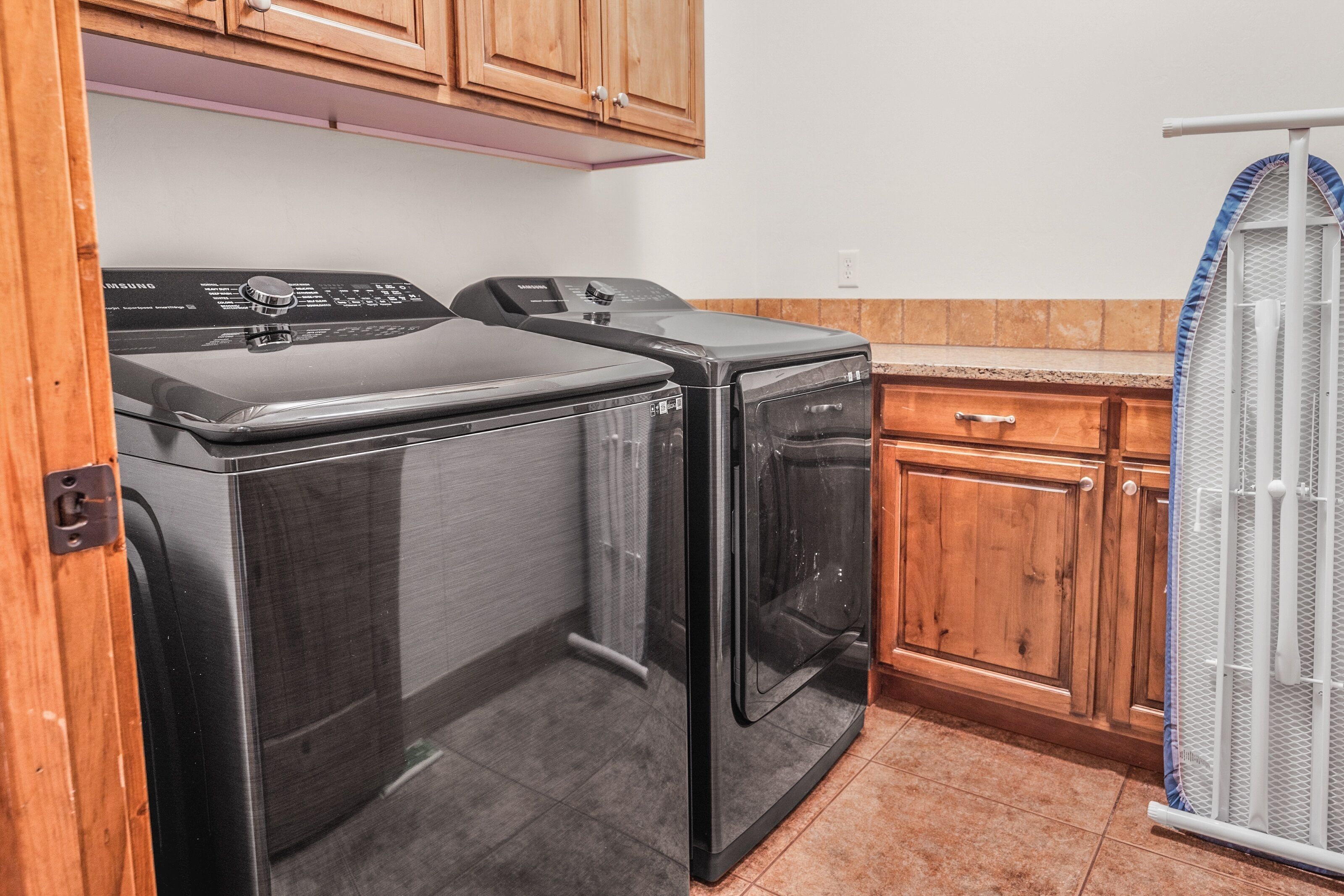 A laundry room with two front-loading washers and dryers, wooden cabinets, and a metal drying rack.