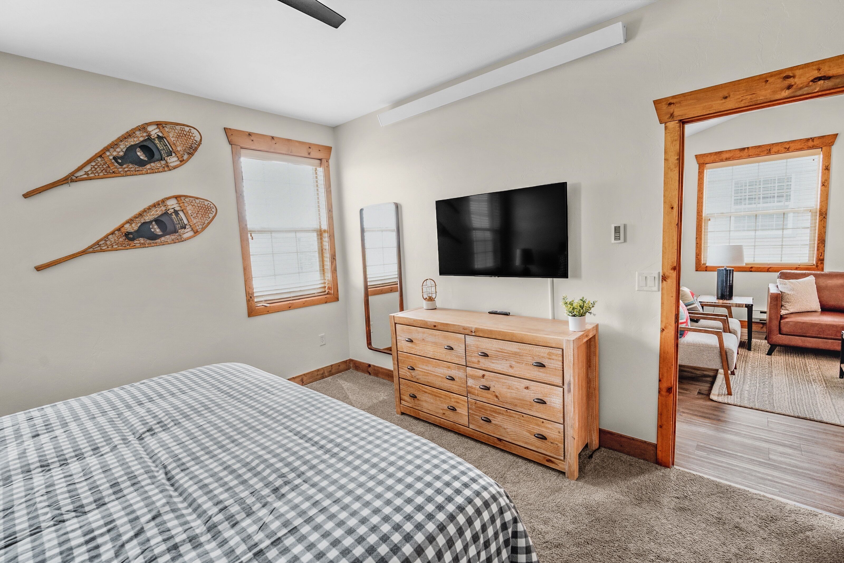 A bedroom with a bed, wooden dresser, TV, and two windows.
