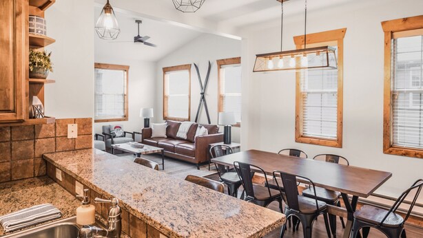 A spacious kitchen with granite countertops, a dining area with a wooden table and chairs, and a cozy seating area with a brown leather sofa. - Teton National Park Avails! Great Location, Games, Laundry, & Playround! (Driggs)