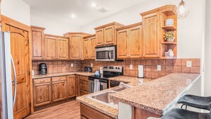 A kitchen with wooden cabinets, a microwave, a stove, a sink, and a granite countertop. - Teton National Park Avails! Great Location, Games, Laundry, & Playround! (Driggs)