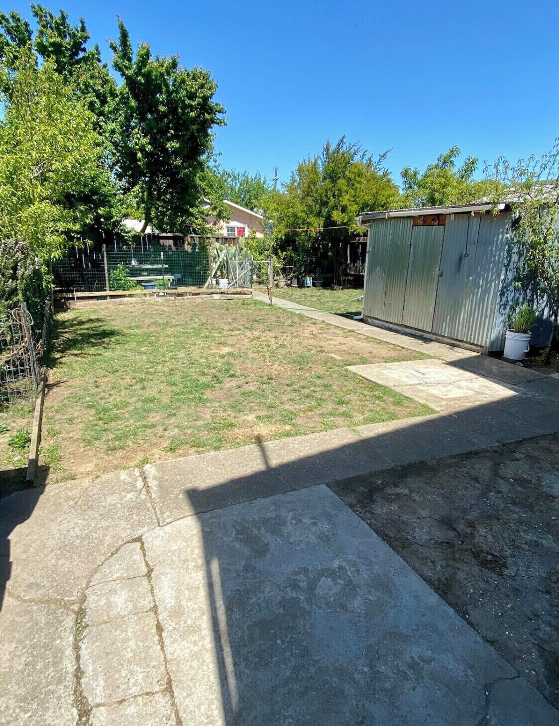 A backyard with a grassy lawn, a metal shed, and a fenced area with a pool.