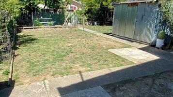 A backyard with a grassy lawn, a metal shed, and a fenced area with a pool.