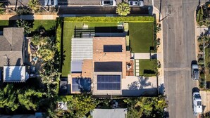 An aerial view of a residential area with a modern house featuring a large solar panel, a swimming pool, and a well-maintained garden. - Cozy Private Beach House - Steps from the beach (Oceanside)