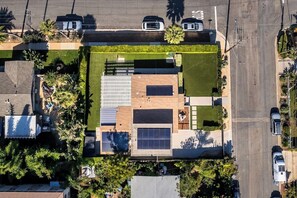 Vue aérienne d’un quartier résidentiel avec une maison moderne dotée d’un grand panneau solaire, d’une piscine et d’un jardin bien entretenu.