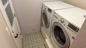 A laundry room with two washing machines, a door, and patterned floor tiles. - Cozy Private Beach House - Steps from the beach (Oceanside)