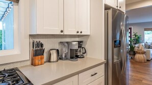 A modern kitchen with white cabinets, a stainless steel refrigerator, a coffee maker, and a gas stove. - Cozy Private Beach House - Steps from the beach (Oceanside)