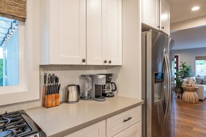 Une cuisine moderne avec des meubles blancs, un réfrigérateur en acier inoxydable, une machine à café et une cuisinière à gaz.