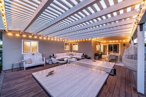 Une terrasse extérieure avec une table de ping-pong, un coin salon et des guirlandes lumineuses.