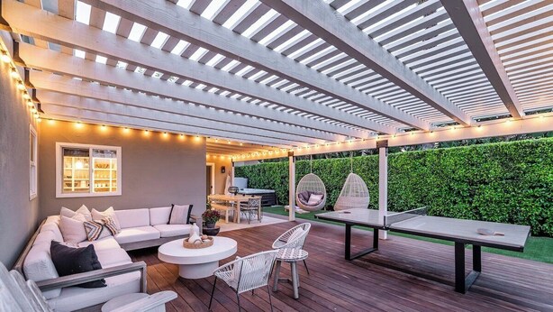 An outdoor patio with a wooden deck, white furniture, a hanging chair, and a table.