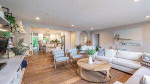 Un vaste espace de vie doté d’un plancher en bois, d’une table basse ronde et d’un canapé. Au fond, on aperçoit une cuisine équipée d’appareils électroménagers modernes, ainsi qu’un coin repas avec des chaises.