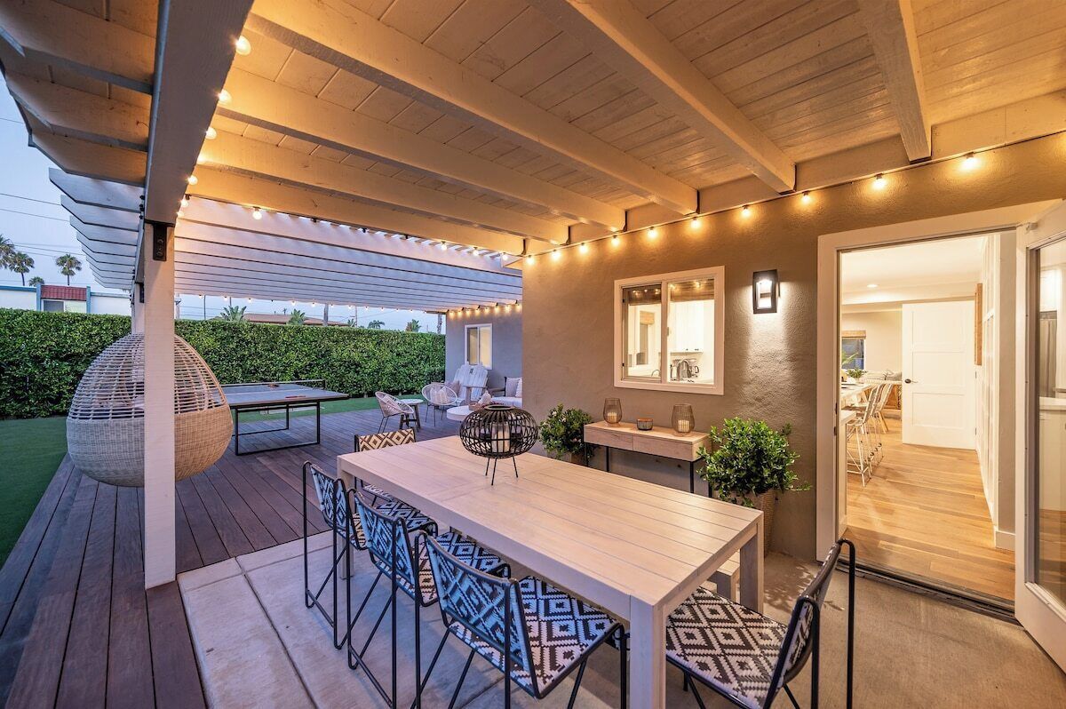 An outdoor patio with a wooden table and chairs, string lights, and a pergola.
