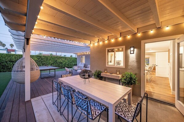 An outdoor patio with a wooden table and chairs, string lights, and a pergola.