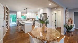 A modern kitchen with white cabinetry, a central island, and a dining area with a glass table.