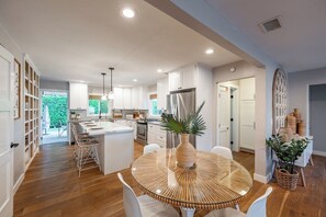 Une cuisine moderne avec des meubles blancs, un îlot central et un coin repas doté d’une table en verre.