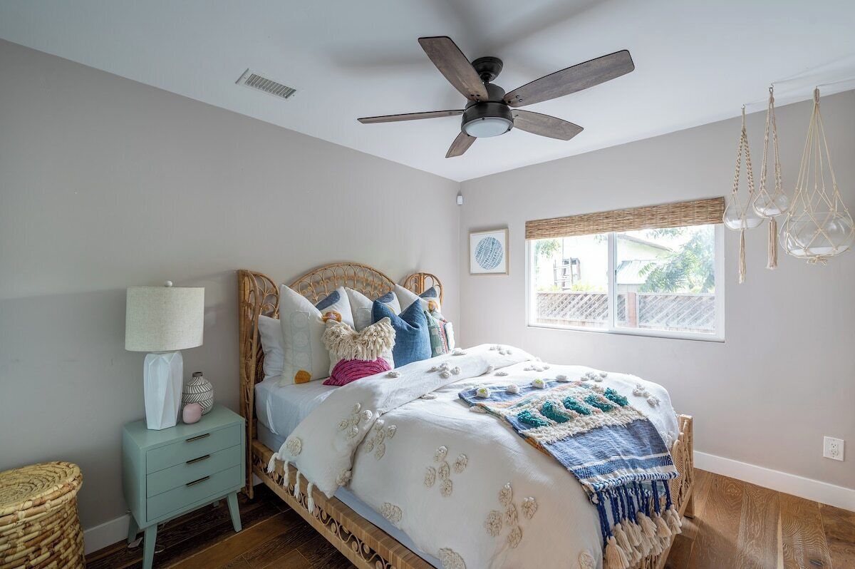 Un dormitorio con cama, mesita de noche, ventilador de techo, ventana con vistas y lámpara colgante.