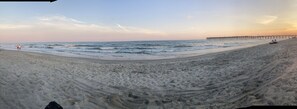 Ein Strand mit einem Steg, der sich ins Wasser erstreckt, sandigem Untergrund und ein paar Spaziergängern.