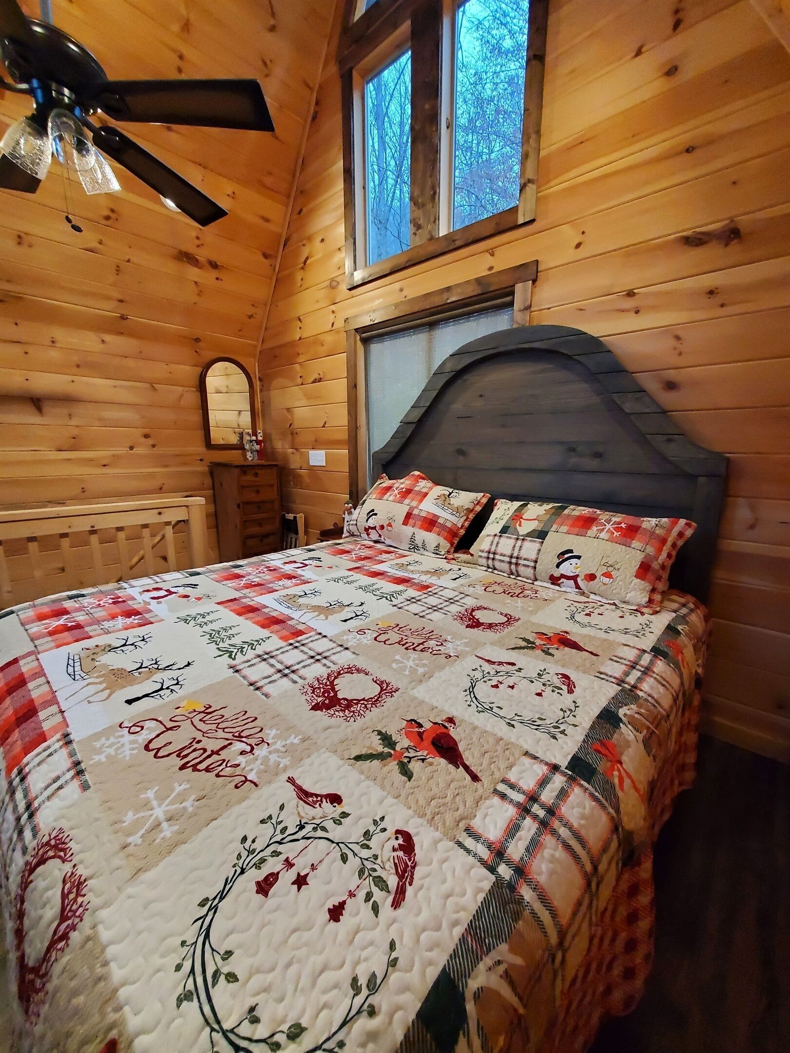 Une chambre confortable dans un chalet en bois, avec un lit, un ventilateur de plafond, une fenêtre et une commode.
