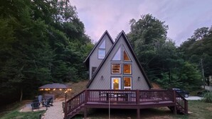 Une cabane à deux étages avec une terrasse, entourée d’arbres.