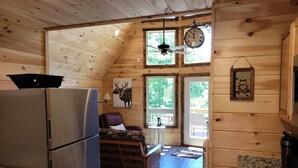 L’intérieur chaleureux de ce chalet comprend un coin cuisine équipé d’un réfrigérateur, une table à manger avec des chaises, un ventilateur de plafond et une grande horloge.