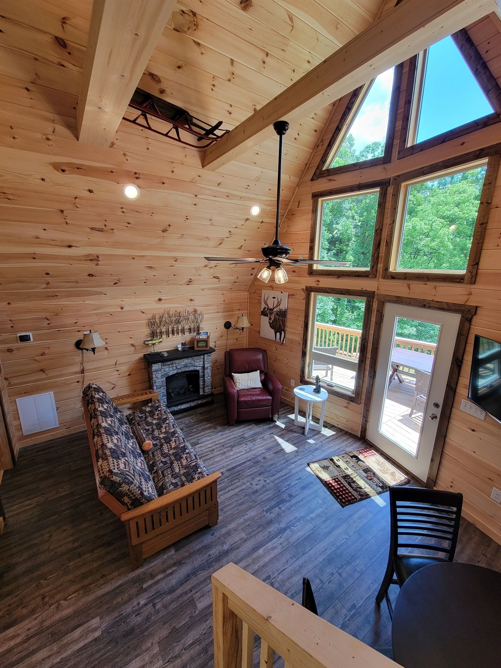 Un interior de cabaña acogedor, con techo de madera, chimenea, sofá, sillón y una mesa de comedor.