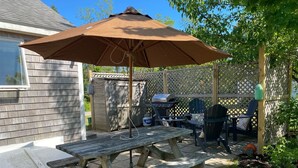Un patio in legno con tavolo da picnic e ombrellone, un barbecue e posti a sedere all'aperto.