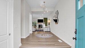 A modern hallway with wooden flooring, a round table with a lamp, and a blue door. - Spacious Modern Townhouse w/Private Rooftop Deck (Arvada)