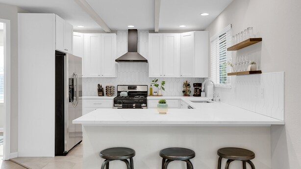 A modern kitchen with white cabinetry, a central island with stools, a built-in stove, and a range hood. - Spacious Modern Townhouse w/Private Rooftop Deck (Arvada)