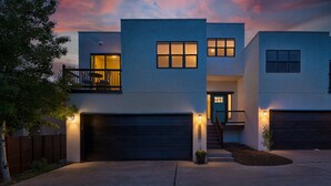 A modern two-story house with a garage, a balcony, and a well-lit entrance. - Spacious Modern Townhouse w/Private Rooftop Deck (Arvada)