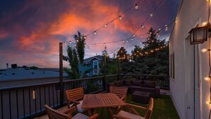 An outdoor patio with a wooden table and chairs, string lights, and a view of a house in the background. - Spacious Modern Townhouse w/Private Rooftop Deck (Arvada)