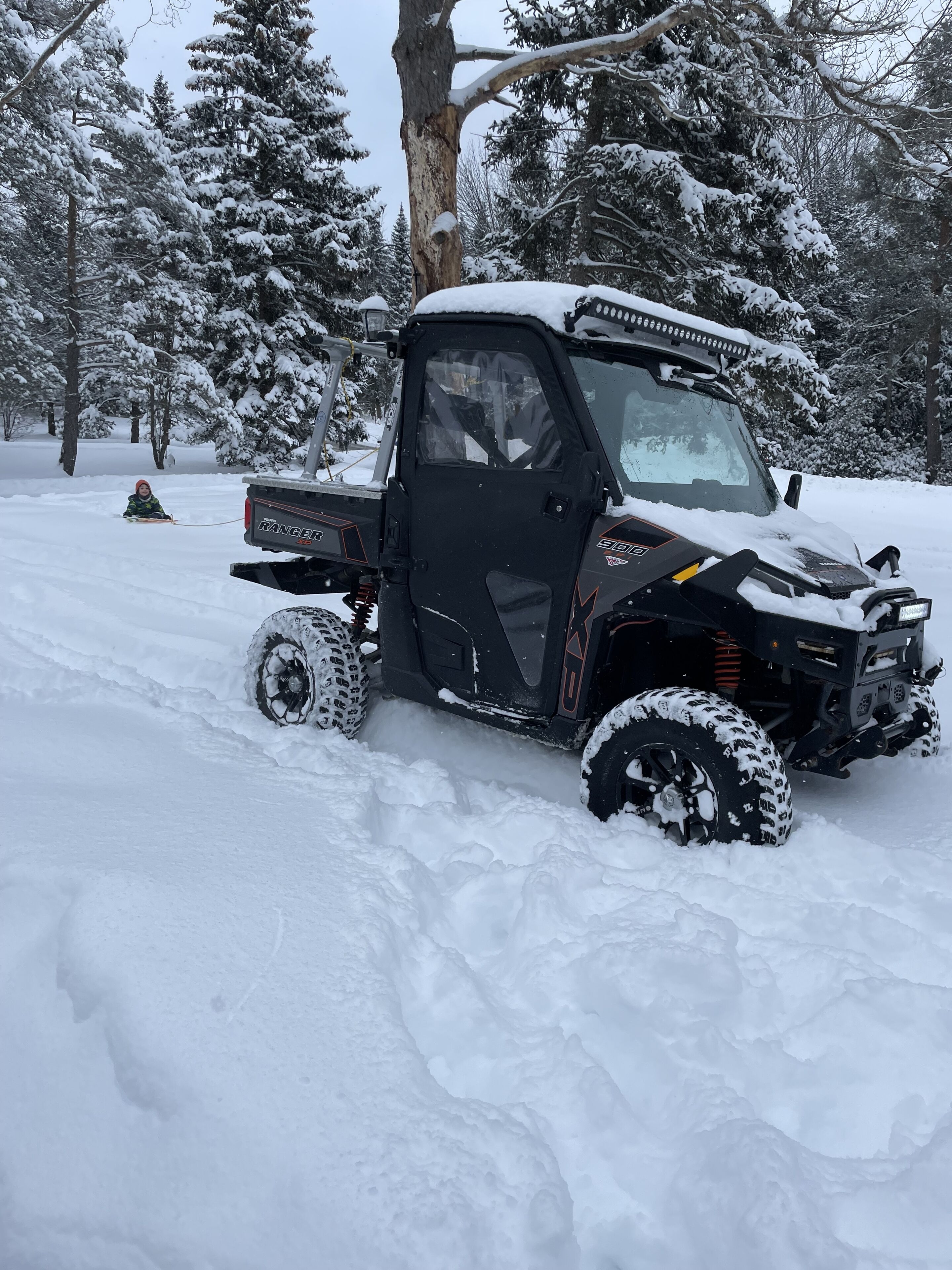 Un veicolo fuoristrada nero con pneumatici ricoperti di neve e un verricello, parcheggiato in una foresta innevata.